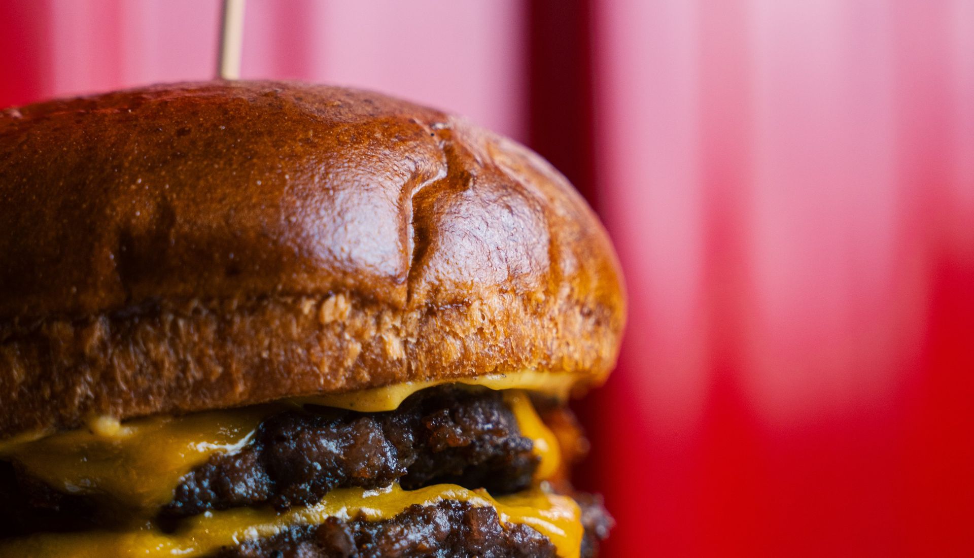 Kırmızı markalı duvarın önünde çift köfteli, cheddarlı smash burger